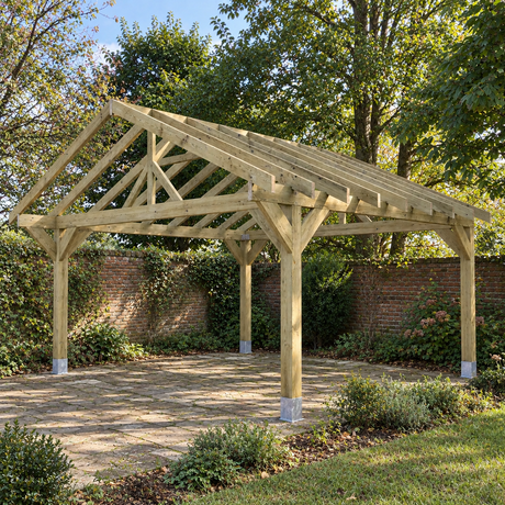 A large wooden gazebo frame with chunky posts  and a pitched roof and open side panels, shown installed on a paved patio in a landscaped UK garden with trees, shrubs, and a brick wall.