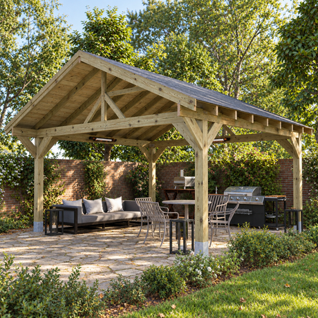 A large heavy duty wooden gazebo with a dark gray felt shingle roof, shown in a landscaped UK back garden with a stone patio, outdoor dining set, sofa, grill, and trees.