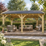 A large wooden garden gazebo with a dark shingle roof shelters an outdoor seating area with wicker sofas, a coffee table, and a hanging egg chair, set in a landscaped garden.