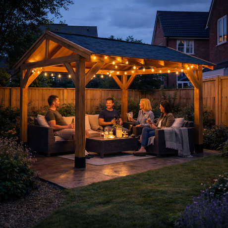 People sitting around enjoying a social evening under a wooden gazebo with festoon lighting at night.