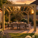 A heavy duty wooden box pergola with integrated string lights stands over a dining table and chairs in a landscaped backyard patio setting at sunset.