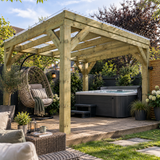 A large wooden pergola with aclear roof over a raised outdoor patio, featuring a dark gray hot tub, a hanging wicker egg chair, and a small table in a landscaped back garden.